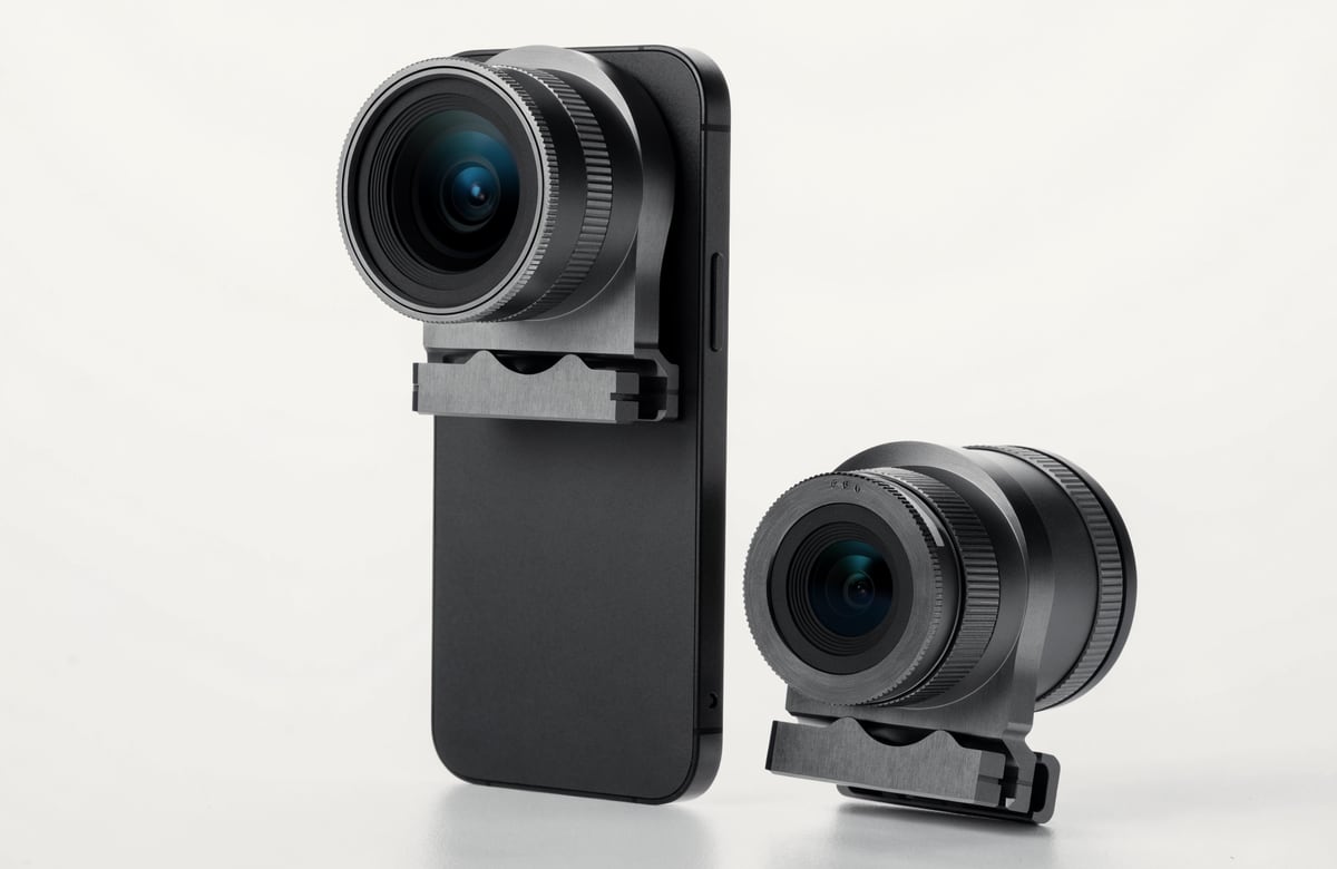 Product photograph: the clip-on camera module mounted to the back of a phone by a rigid machined clamp, with a second module detached alongside showing its large multi-element lens, knurled focus ring and rear contact plate.